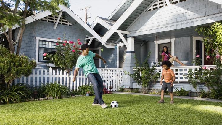 Father and son playing soccer on the front lawn while mom watches from the porch. 